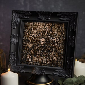 May include: A black framed picture with a gold-toned image of a creature with a human face surrounded by branches. The picture is on a black stand and there are two candles on either side of it.