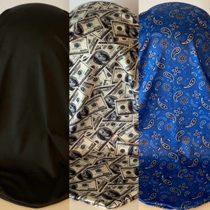 Könnte beinhalten: Drei Satin-Kissenbezüge, einer schwarz, einer mit einem Muster aus US-Dollar-Scheinen und einer mit einem blauen Paisley-Muster.