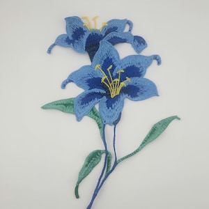 May include: Blue embroidered flower patch with green leaves. The flower has a yellow center.