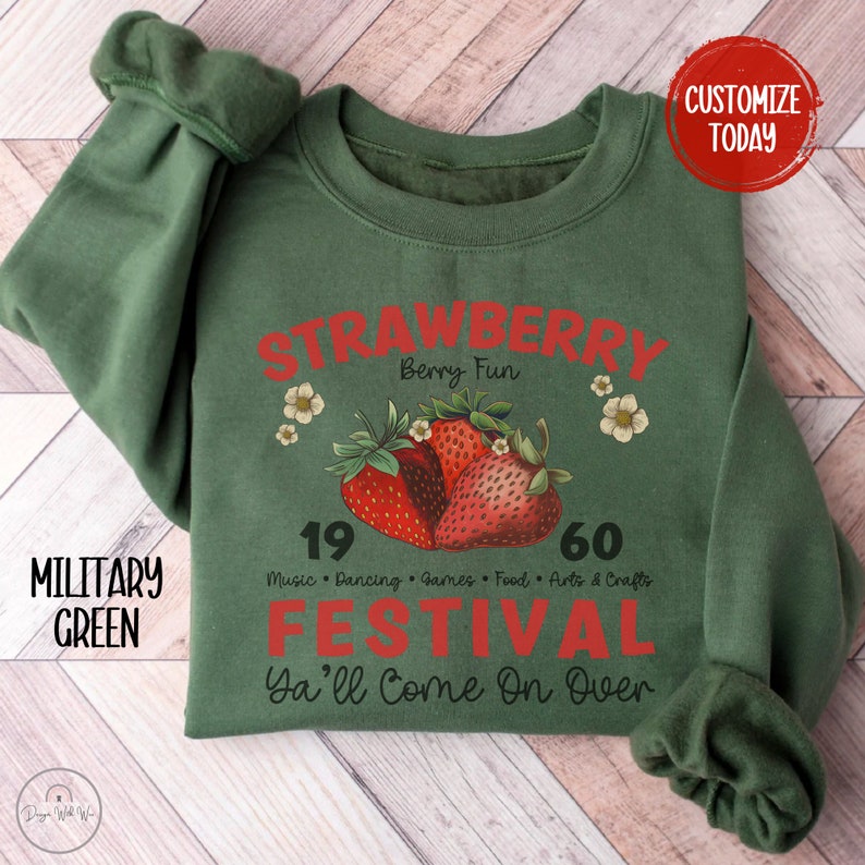 May include: A green sweatshirt with a red graphic design that says "Strawberry Berry Fun 19 60 Music Dancing Games Food Arts & Crafts Festival Ya'll Come On Over". The graphic also features a cluster of red strawberries.