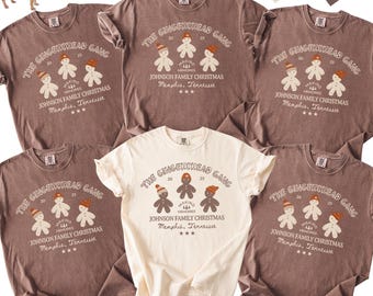 May include: A collection of t-shirts in espresso and ivory colors, featuring a gingerbread family graphic with the text "The Gingerbread Gang" and "Johnson Family Christmas, Memphis, Tennessee". Matching pet bandana available.