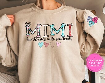 May include: Beige sweatshirt with the text "this MIMI has the cutest little sweethearts" and five small patterned hearts. The sleeve has the text "James, Chloe, and Ava" in pink, blue, and purple hearts.