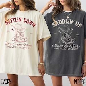 May include: Two oversized t-shirts with a vintage-inspired design. The ivory t-shirt features the text "Settlin' Down" with a cowboy boot graphic and the text "Same Cowboy Forever" and "Nashville, Tennessee". The gray t-shirt features the text "Saddlin' Up" with a cowboy boot graphic and the text "Olivia's Last Rodeo" and "Nashville, Tennessee".