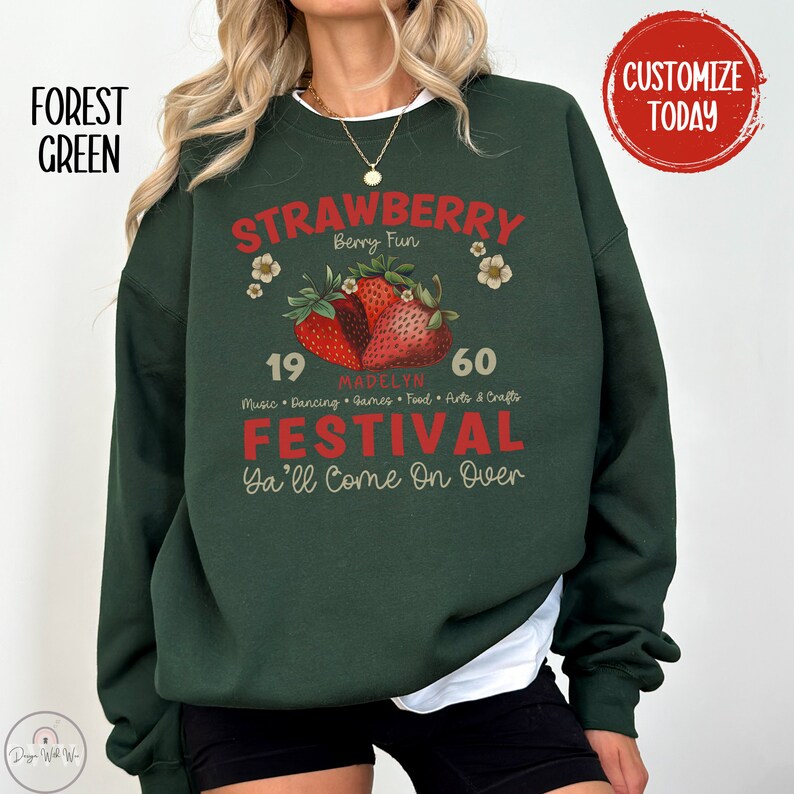 May include: A forest green sweatshirt with a vintage-style graphic design featuring a strawberry festival. The design includes the text "Strawberry Berry Fun", "Madelyn", "19", "60", "Music Dancing Games Food Arts & Crafts", "Festival", and "Ya'll Come On Over".