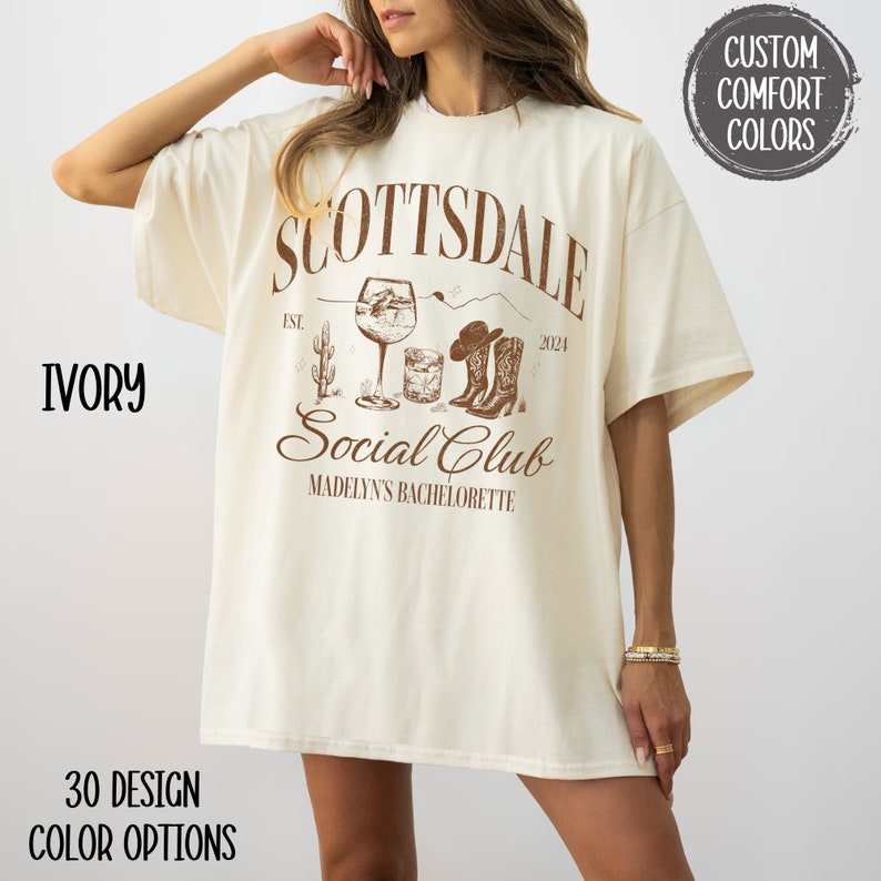 May include: Ivory oversized t-shirt with a brown graphic design that says "Scottsdale Social Club" with a cactus, cowboy boots, and a cocktail glass. The text also says "Est. 2024" and "Madelyn's Bachelorette".