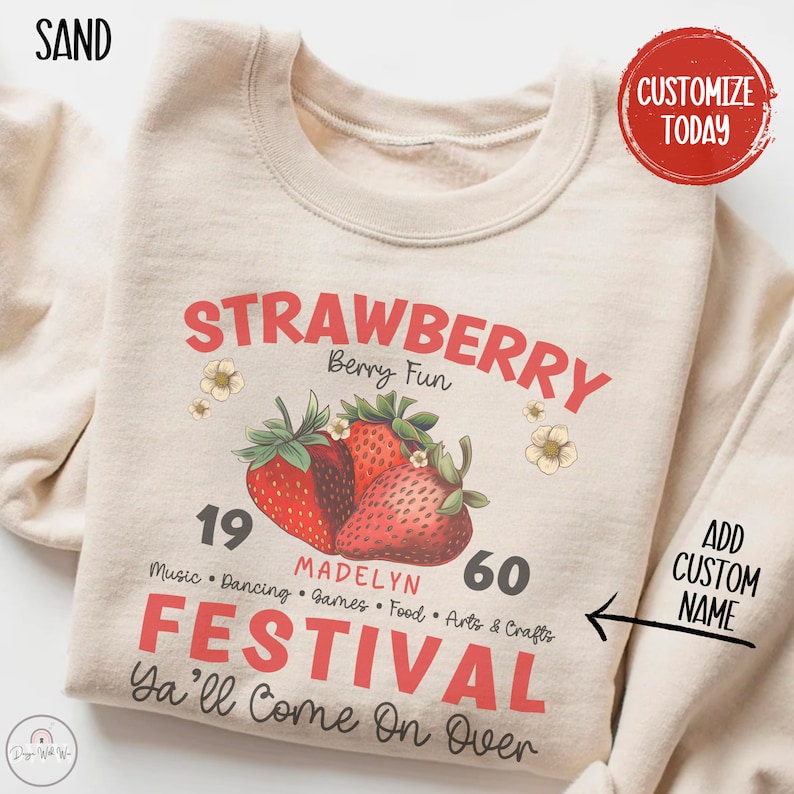 May include: A beige sweatshirt with a graphic design of strawberries and the text "STRAWBERRY Berry Fun 19 MADELYN 60 FESTIVAL Ya'll Come On Over" in red and black. The text "ADD CUSTOM NAME" is also included on the sweatshirt.