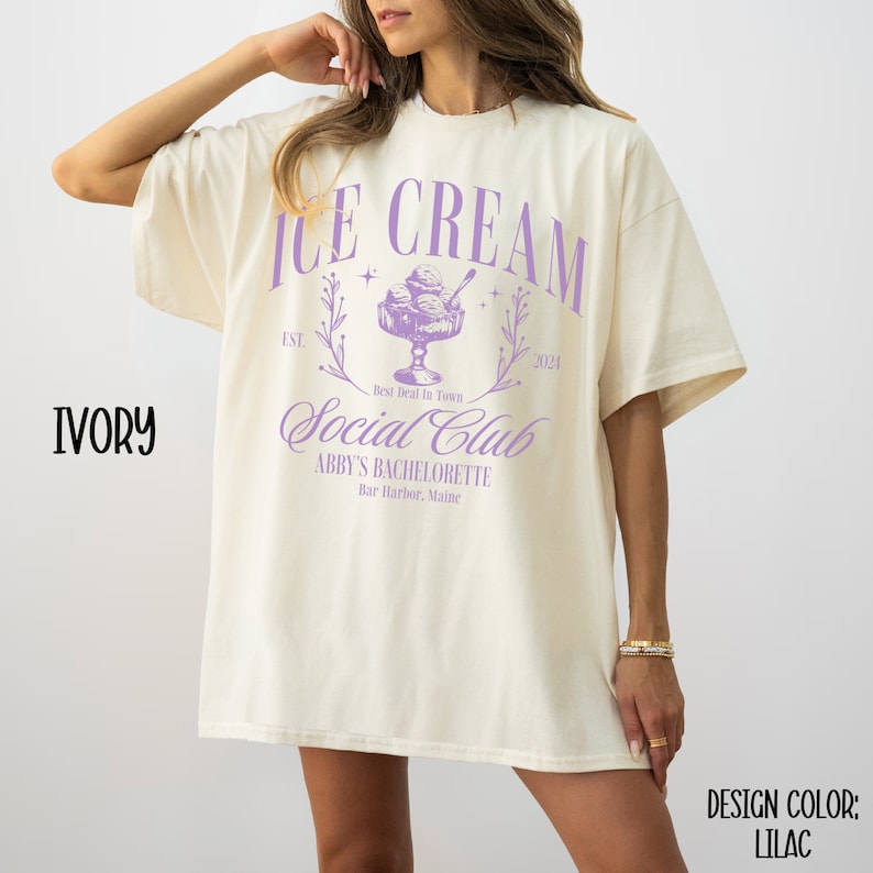 May include: A white t-shirt with a purple graphic design that says "Ice Cream Social Club" with a vintage-style ice cream cone and the text "Abby's Bachelorette" and "Bar Harbor, Maine".