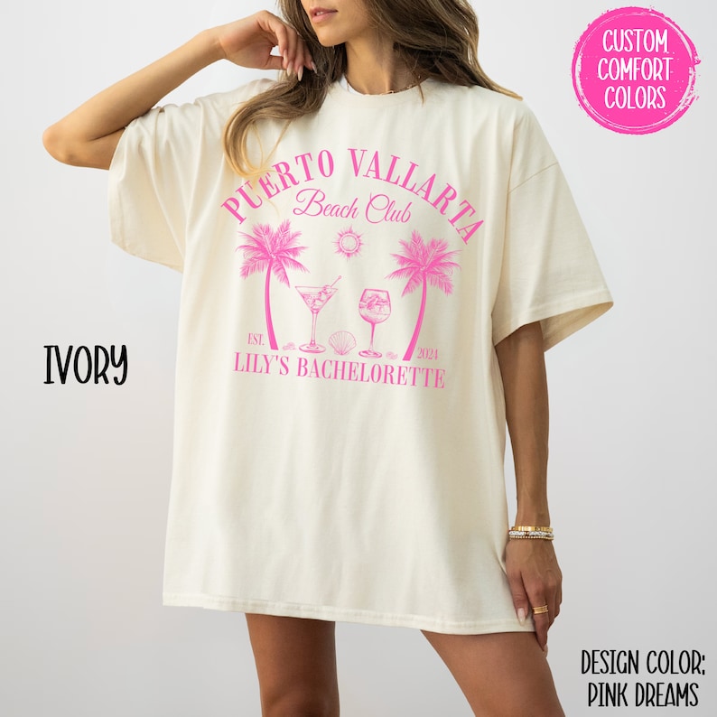 Pu&ograve; includere: Una maglietta bianca con un design grafico rosa che dice "Puerto Vallarta Beach Club" con palme, bevande e il testo "Est. 2024 Lily's Bachelorette".