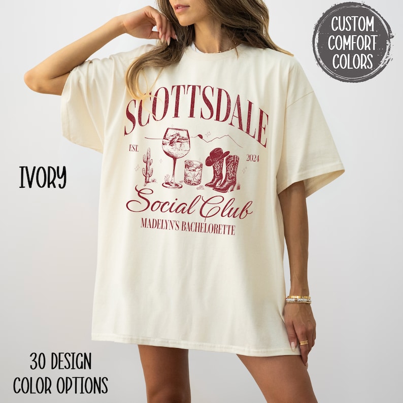 May include: A white t-shirt with a red graphic design that says "Scottsdale Social Club" with a wine glass, cactus, and cowboy boots. The text "Est. 2024" and "Madelyn's Bachelorette" are also included in the design.
