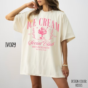 May include: Ivory t-shirt with a pink graphic design that says "Ice Cream Social Club" with a vintage ice cream cone illustration and the text "Est. 2024" and "Abby's Bachelorette, Bar Harbor, Maine".