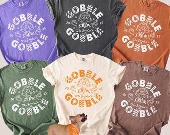 May include: A collection of six colorful t-shirts with the word "GOBBLE" in a circular design, along with the text "CREW" and "The Jordan's". The shirts are in various colors, including purple, gray, orange, green, cream, and brown. A matching pet bandana is also shown.