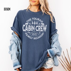 May include: A denim blue t-shirt with a white graphic that reads "The Tolman Cabin Crew Family Reunion 2025". The design includes bears, trees, and the words "Making Memories". The shirt is a relaxed fit.