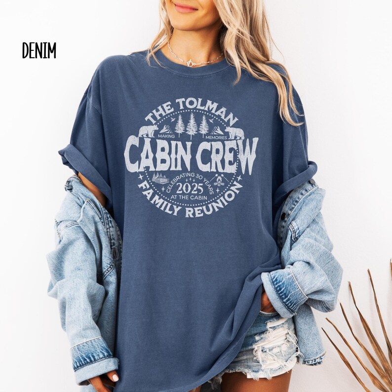 May include: A denim blue t-shirt with a white graphic that reads "The Tolman Cabin Crew Family Reunion 2025". The design includes bears, trees, and the words "Making Memories". The shirt is a relaxed fit.