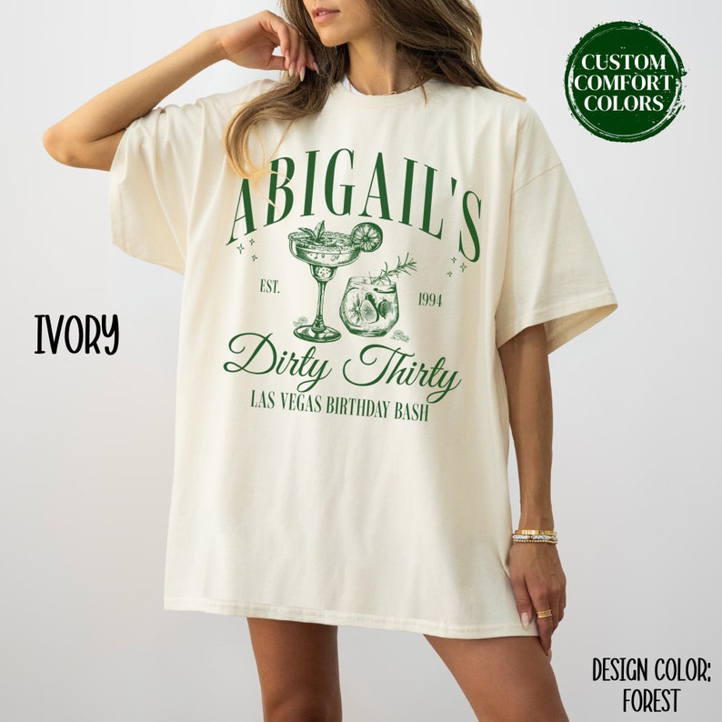 Pode incluir: Uma camiseta branca com o texto "Abigail's Dirty Thirty Las Vegas Birthday Bash" em verde. O design inclui dois copos de coquetel com uma guarni&ccedil;&atilde;o de lim&atilde;o e alecrim. O texto "Est. 1994" tamb&eacute;m est&aacute; inclu&iacute;do no design.