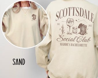 May include: Sand-colored sweatshirt with the text "Scottsdale Social Club Maddie's Bachelorette" and a graphic of a cactus, boots, and a cocktail glass. The text "Est. 2025" is also included.