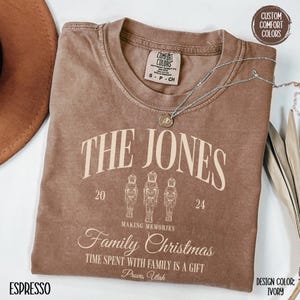 May include: A brown t-shirt with a vintage-style design featuring the text "The Jones" with a nutcracker motif. The text "Making Memories Family Christmas" is below the nutcrackers. The text "Time Spent With Family Is A Gift" is below the Christmas text. The text "Provo, Utah" is below the previous text. The design color is ivory.