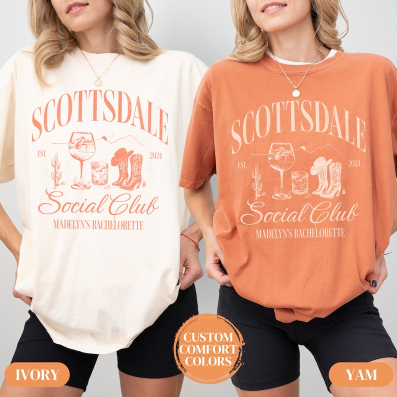 May include: Two women wearing oversized t-shirts with the text "Scottsdale Social Club" and the year "2024". The shirts are in ivory and yam colors. The text is in a vintage style font. The shirts feature a graphic of a cactus, a glass of wine, a cowboy hat, and cowboy boots.