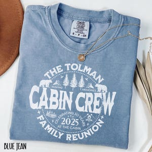 May include: A blue jean Comfort Colors t-shirt with a white graphic that reads "The Tolman Cabin Crew Family Reunion 2025." The design includes bears, trees, and the text "Making Memories." A gold necklace with a pendant rests on the shirt.