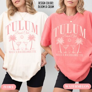 Pu&ograve; includere: Due donne indossano magliette oversize con il testo "Tulum Beach Club" in rosa. Le magliette sono di colore avorio e cocomero. Il testo "EST. 2021 MAYA'S BACHELORETTE" &egrave; stampato sotto il testo principale.