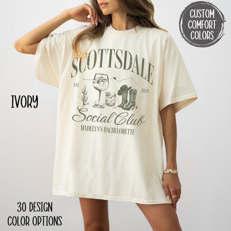 May include: Ivory oversized t-shirt with a graphic design featuring the text "Scottsdale Social Club" with a cactus, a glass of wine, a cocktail glass, and cowboy boots. The text "Est. 2024" and "Madelyn's Bachelorette" are also included in the design.