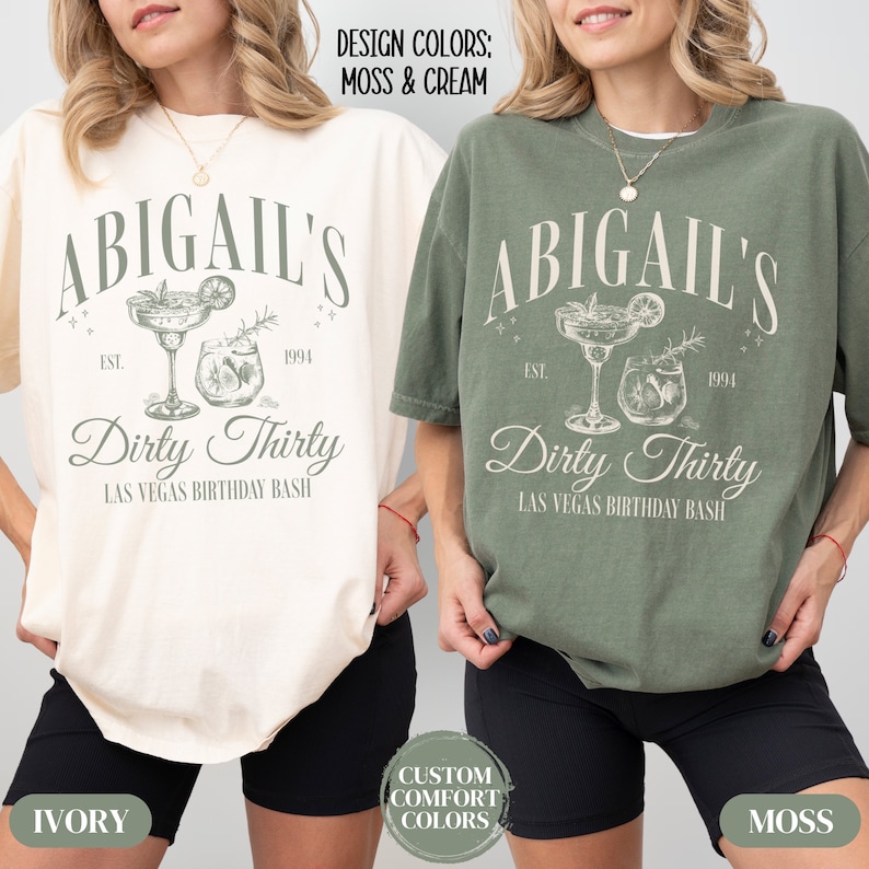 Pode incluir: Duas mulheres vestindo camisetas com o texto "Abigail's Dirty Thirty Las Vegas Birthday Bash" em uma fonte de estilo vintage. As camisetas s&atilde;o nas cores marfim e verde musgo. O texto &eacute; cercado por um gr&aacute;fico de dois coquet&eacute;is.