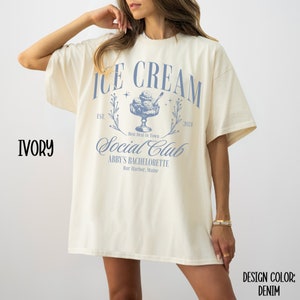 May include: Ivory t-shirt with a blue graphic design that says "Ice Cream Social Club" with the text "Est. 2024" and "Abby's Bachelorette Bar Harbor, Maine".