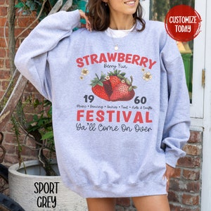 May include: Grey sweatshirt with a red and white strawberry graphic. The text "STRAWBERRY Berry Fun" is above the strawberries. The text "19 60 Music Dancing Games Food Arts & Crafts FESTIVAL Ya'll Come On Over" is below the strawberries.