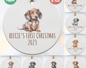 May include: Twelve dachshund puppies are featured on a set of ten round, white ceramic Christmas ornaments. Each ornament features a different dachshund puppy with the text "[puppy's name]'s First Christmas 2023".
