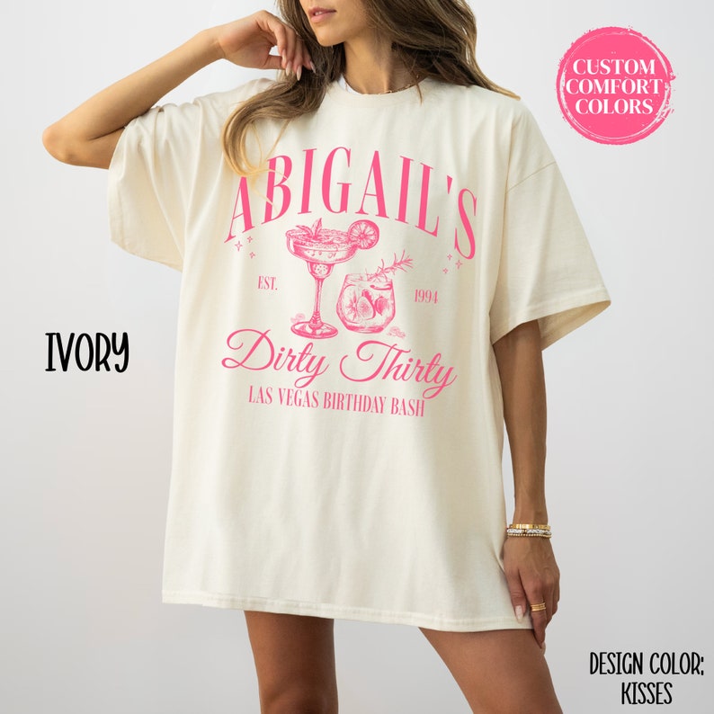Pode incluir: Uma camiseta branca com um design gr&aacute;fico rosa que diz "Abigail's Dirty Thirty Las Vegas Birthday Bash" com uma ilustra&ccedil;&atilde;o de coquetel. O texto "Est. 1994" tamb&eacute;m est&aacute; inclu&iacute;do no design.