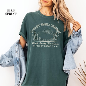 May include: A dark teal t-shirt with the text "CORLEY FAMILY REUNION" above a mountain and tree graphic. Below the graphic is "Great Smoky Mountains" and "Pigeon Forge, TN". The shirt is a solid color and has short sleeves.