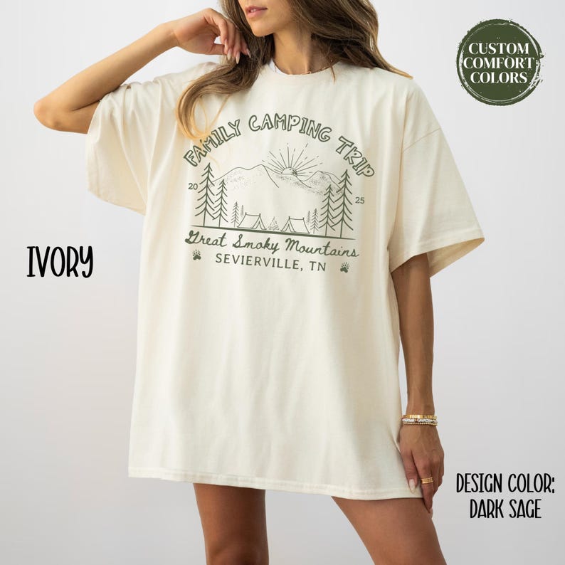 May include: Ivory-colored t-shirt with a "Family Camping Trip" graphic featuring mountains, trees, and the text "Great Smoky Mountains, Sevierville, TN." The design includes the numbers 20 and 25. The design color is dark sage.