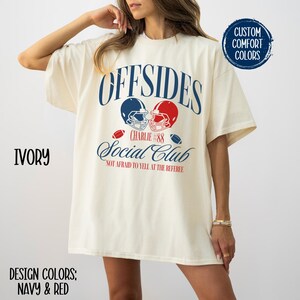 May include: Ivory oversized t-shirt with a graphic design of two football helmets colliding. The text reads "Offsides Charlie #88 Social Club Not Afraid to Yell at the Referee".
