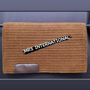 Könnte beinhalten: Ein braunes rechteckiges Sattelpad mit strukturierter Oberfläche. Das Pad hat einen dunkelbraunen Lederfleck unten und den Text "MRS INTERNATIONAL" über die Mitte.