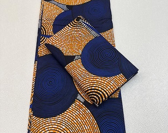 May include: A folded fabric with a repeating pattern of orange and white concentric circles on a navy blue background. A smaller, folded piece of the same fabric is also present. The fabric has a bold, geometric design.