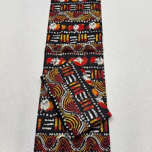 May include: A black fabric with a vibrant pattern featuring red, yellow, and white leaf and wave designs. The fabric is folded, with a smaller piece on top, showcasing the repeating pattern.