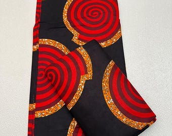 May include: Black fabric with a repeating pattern of red and orange concentric circles. The circles are outlined with a gold-colored border. A folded piece of the same fabric is also present.