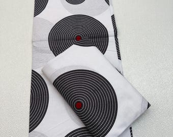 May include: White fabric with a repeating pattern of black and gray concentric circles, each with a red center. A folded piece of the same fabric is also present, showcasing the design.