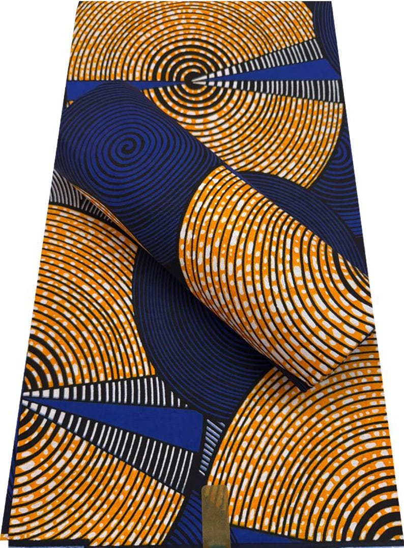May include: A vibrant fabric with a repeating pattern of concentric orange and black circles on a navy blue background. White dotted lines and blue rectangular shapes add contrast. The fabric is rolled up, showcasing the design.
