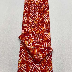 May include: A vibrant red fabric with a white geometric pattern, featuring diamonds, lines, and arrow-like shapes. The fabric is folded, showcasing the design. The text "GUARANTEED BLOCK PRINTS SUPER GLOBAL" is visible at the bottom.