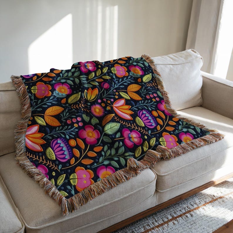 May include: A colorful floral throw blanket with a black background and fringed edges. The blanket features a repeating pattern of pink, orange, yellow, and purple flowers with green leaves.