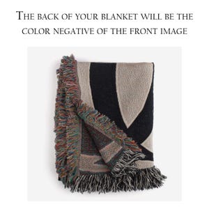 May include: A black and beige woven throw blanket with fringe on all sides. The back of the blanket is a color negative of the front image.