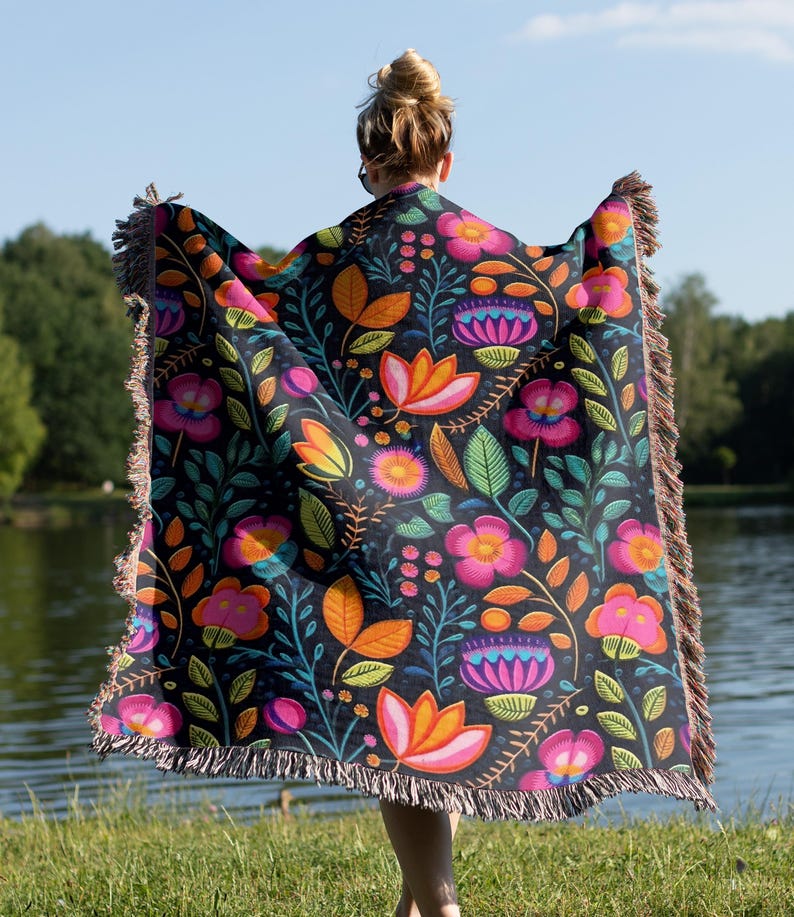 May include: A woven throw blanket with a colorful floral pattern on a black background. The blanket has fringe on all sides.