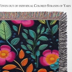May include: A woven tapestry throw blanket with a floral pattern featuring pink, orange, and green flowers on a dark blue background. The blanket has a fringe border.