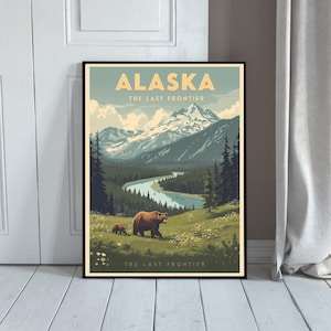 May include: A framed poster featuring the word "ALASKA" in yellow. The image shows a mountain range, a river, and two brown bears in a landscape. The text "THE LAST FRONTIER" is displayed above and below the illustration.