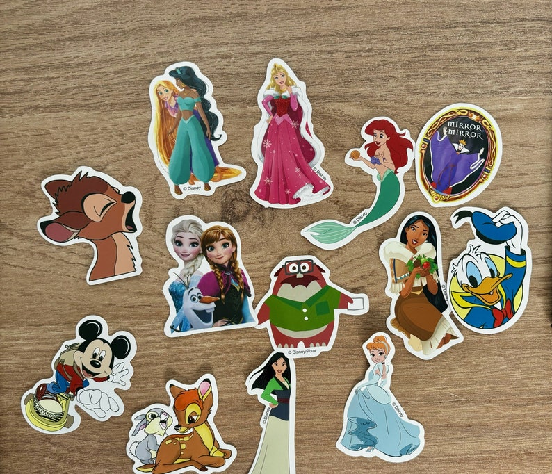 May include: A collection of Disney character stickers featuring princesses, animals, and villains. The stickers are colourful and feature various characters from Disney films, including Cinderella, Snow White, and Mickey Mouse.