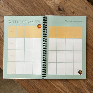 May include: A green weekly organiser with a spiral binding. The cover has the words "Weekly Organiser" and the text "Remember your rest days". There are illustrations of a lion and a beehive.