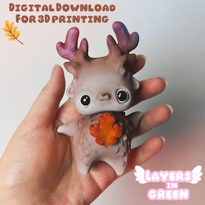 May include: A 3D printed figurine of a small, brown deer with large eyes and a textured surface. The deer is holding a small, orange leaf in its front paws. The figurine is being held in a hand. The text "Layers in Green" is visible in the lower right corner of the image.