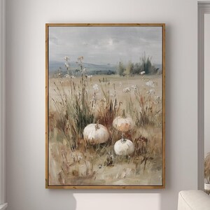 May include: A framed landscape painting depicts a field with pumpkins. The artwork features a neutral color palette with a wooden frame. The painting is hung on a white wall in a room with a window and a modern lamp.