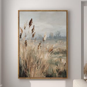 May include: A framed landscape painting shows tall, dried grasses in a field under a muted sky. The artwork is in a wooden frame and hangs on a white wall. A modern stool and lamp are in the foreground.