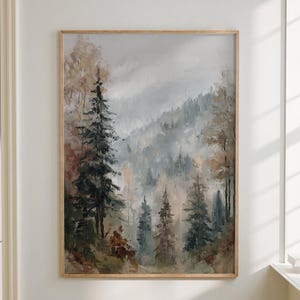 Può includere: Un dipinto di paesaggio incorniciato raffigura una scena di foresta nebbiosa con alti alberi sempreverdi e colori tenui. L'opera d'arte è esposta su una parete bianca sopra un divano e un tavolino di legno. Una lampada verde è su un davanzale.